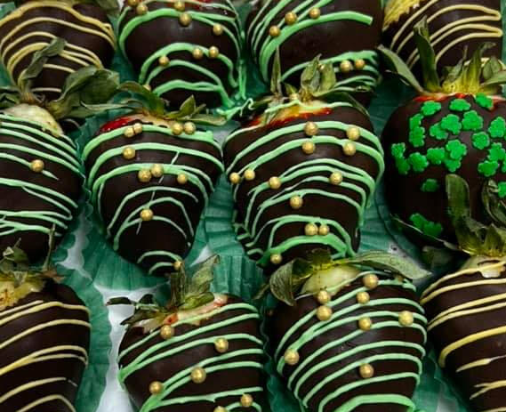 Milk chocolate covered strawberries with green swizzles adorned with gold and clover sprinkles.